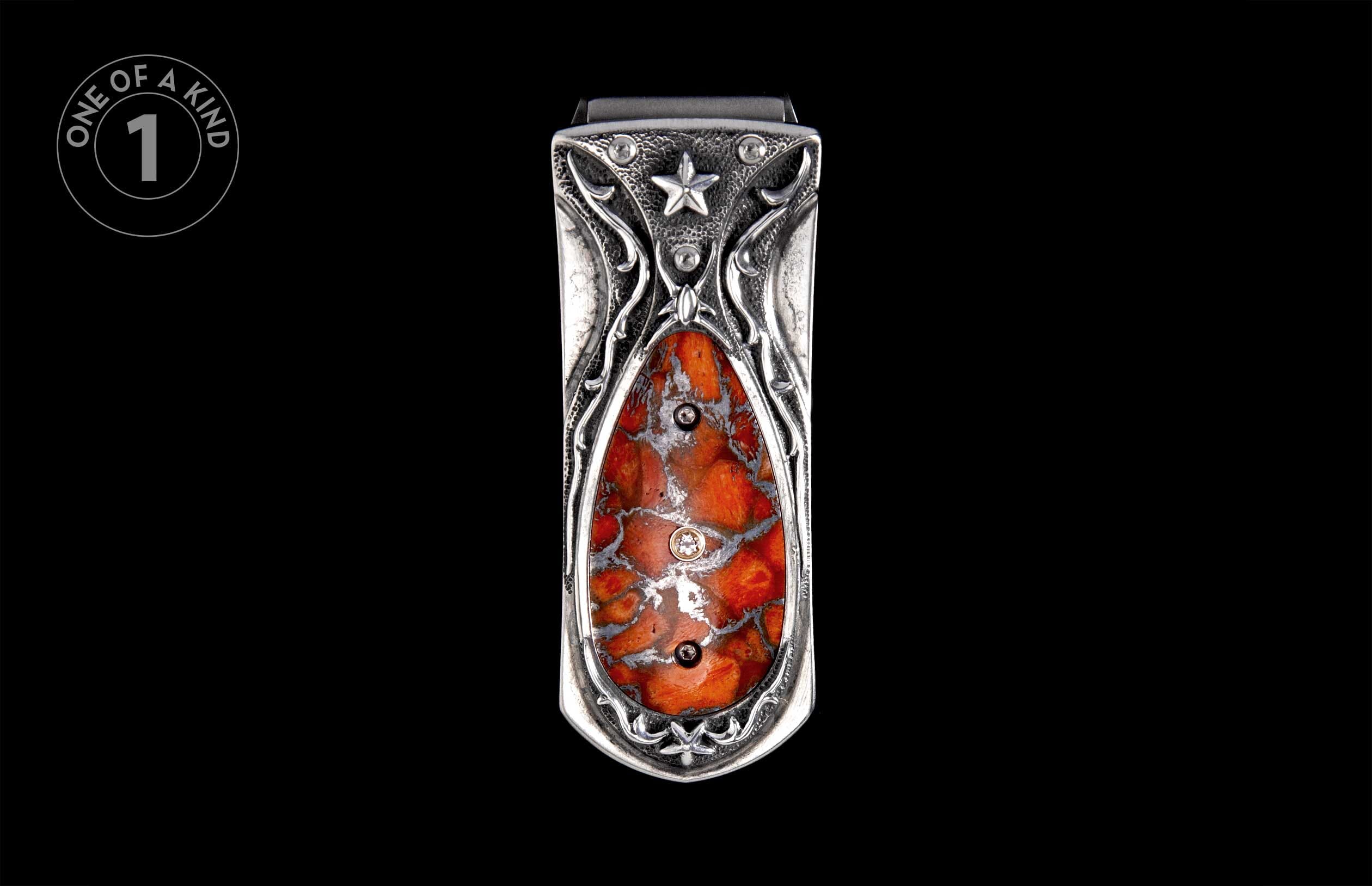 Ornate silver-toned money clip with a central mottled orange and grey stone, featuring scrollwork and a star emblem.