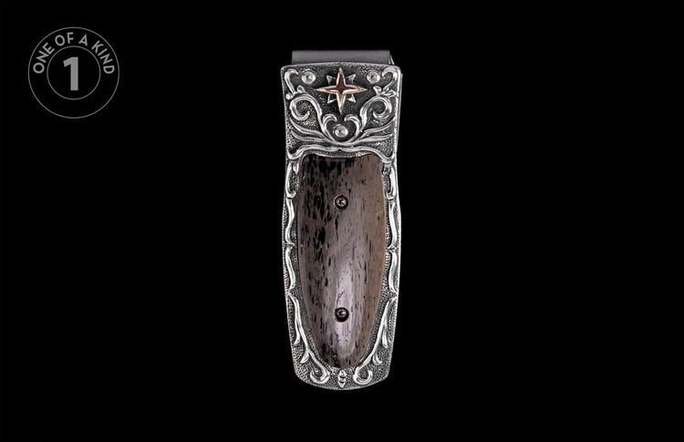 Silver-toned money clip with a pebbled background, dark textured insert, elaborate scrollwork, and a bronze star accent.