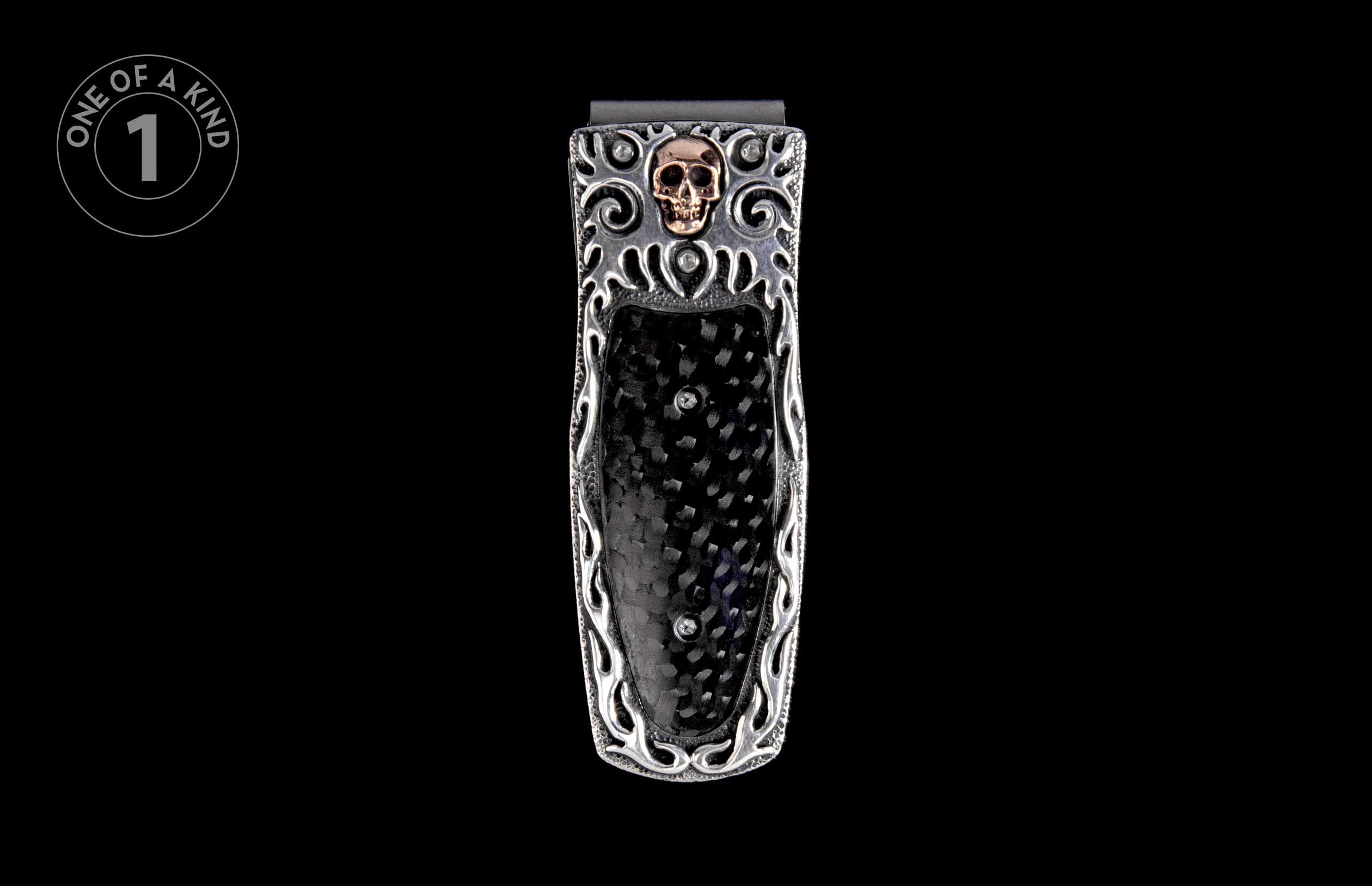 Silver money clip with a gold skull emblem, black carbon fiber inlay, and intricate silver scrollwork.