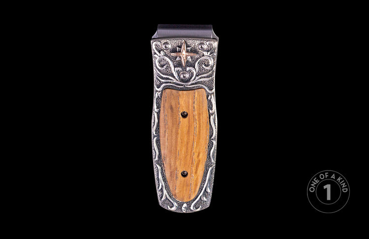 Ornate money clip with a silver-toned frame featuring scrollwork, stippling, a bronzed star, and a central polished brown wood inlay.