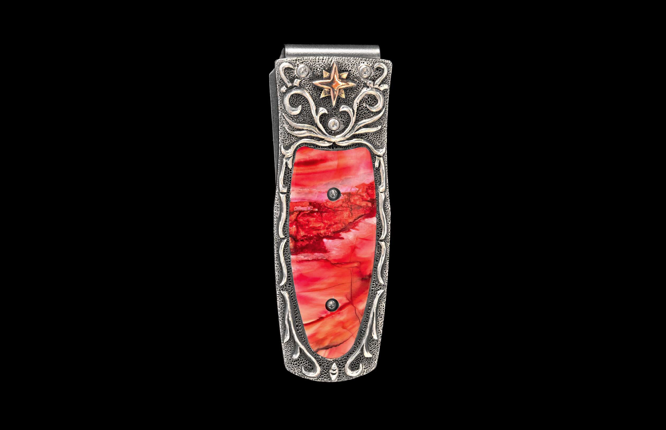 Silver money clip with a vibrant red inlay, adorned with intricate scrollwork, a gold star, and clear stones.