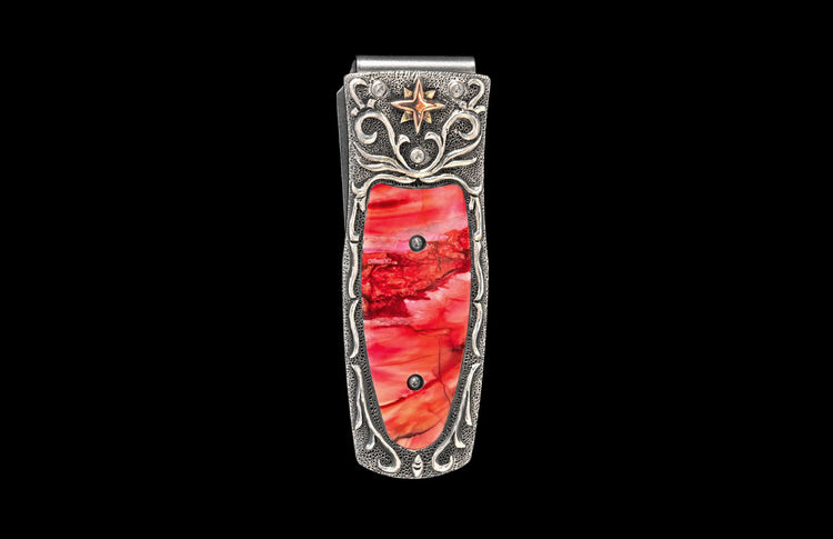 Silver money clip with a vibrant red inlay, adorned with intricate scrollwork, a gold star, and clear stones.
