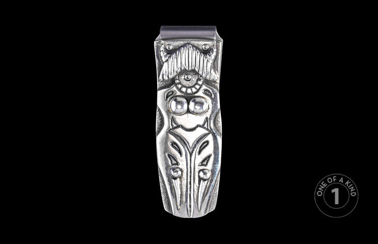 Silver-toned metal money clip with ornate carved design of a stylized figure.