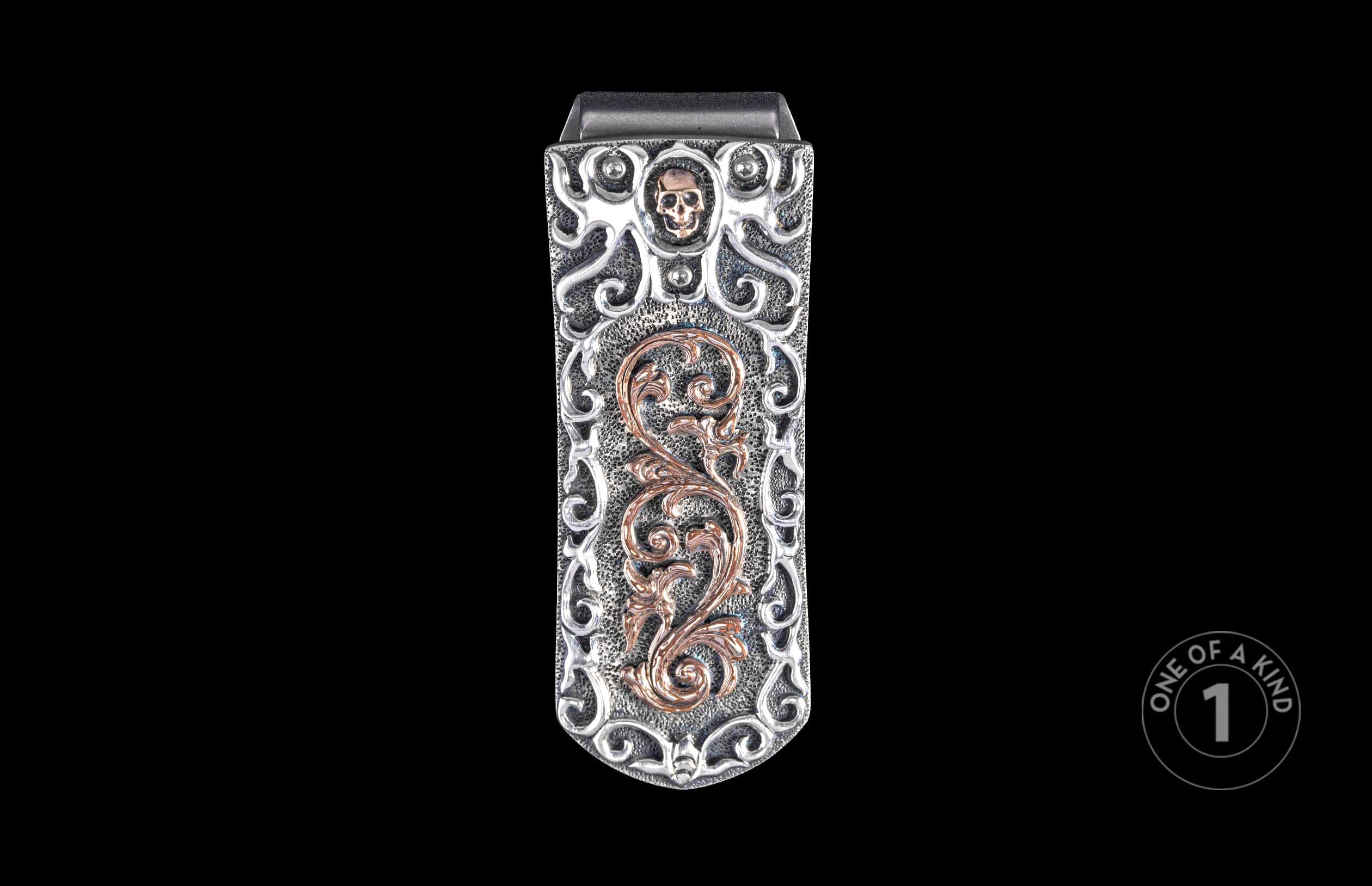 Ornate silver money clip with a copper skull and intricate scrollwork on a textured base.