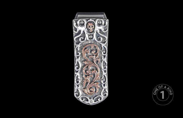 Ornate silver money clip with a copper skull and intricate scrollwork on a textured base.