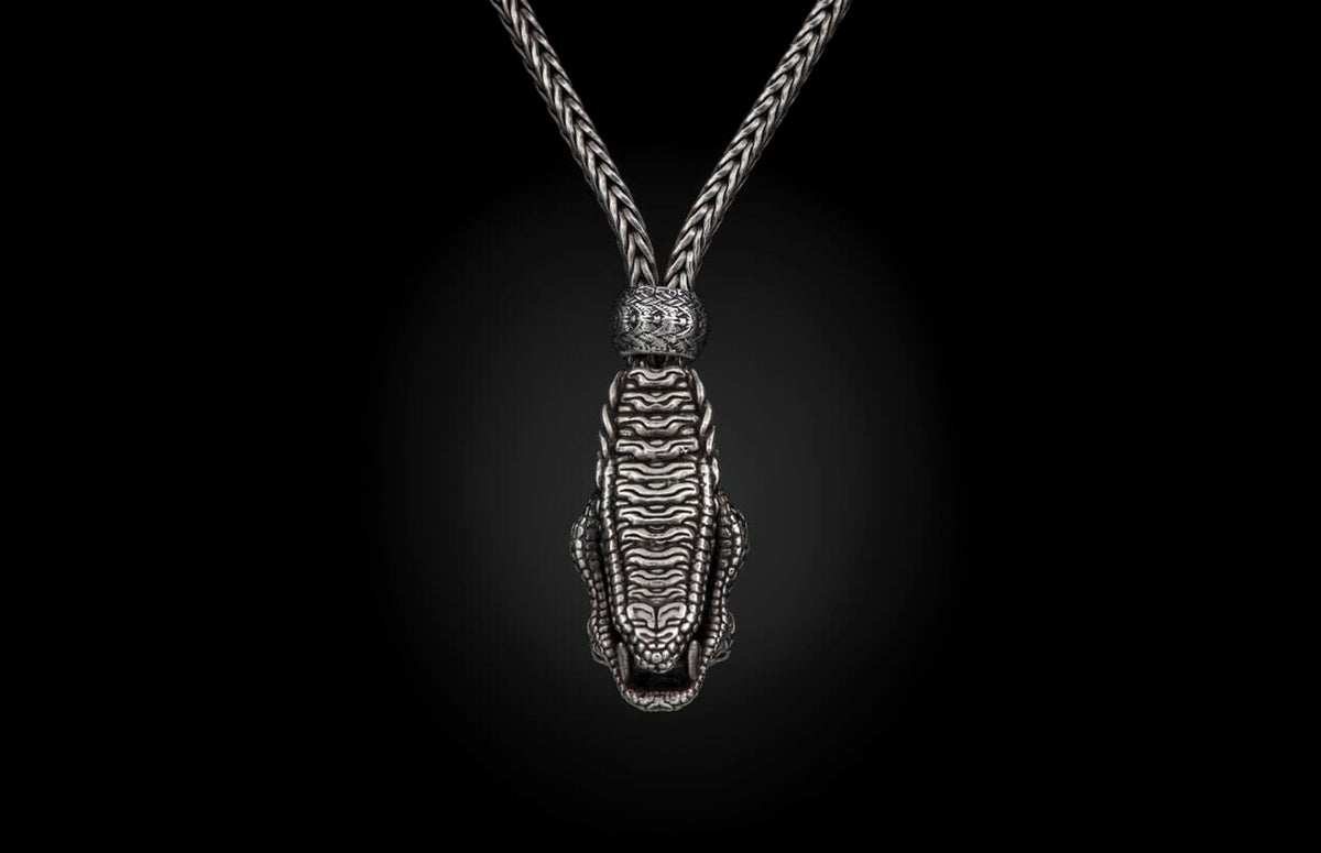 Silver-toned braided necklace featuring a detailed crocodile head pendant with an open mouth, connected by an ornate bead.