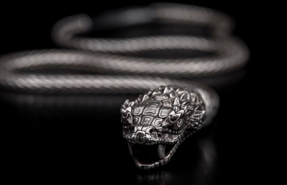 Silver-toned snake head bracelet with detailed scales, open mouth, fangs, and braided coiled body.