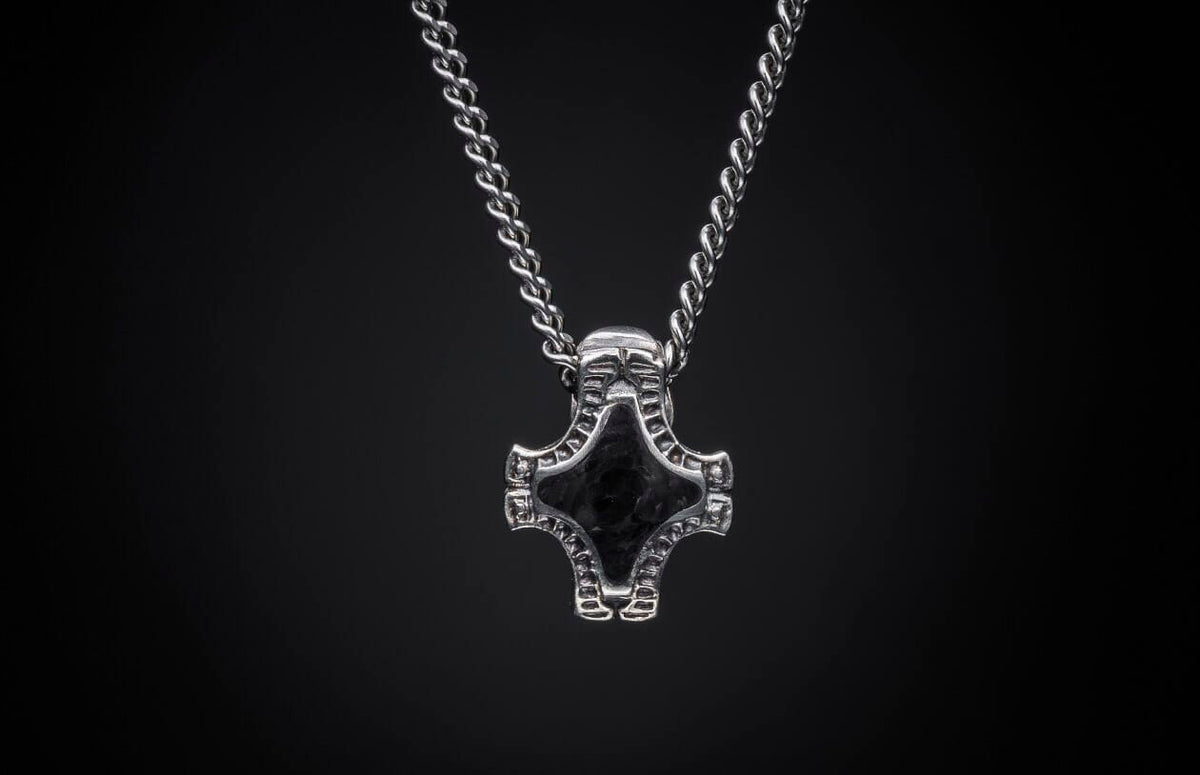 Silver chain necklace with a textured, hammer-shaped pendant featuring a dark center inlay.