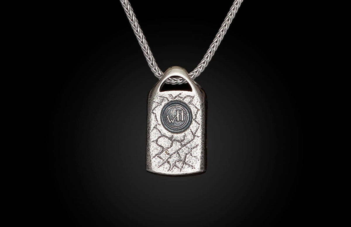 Silver necklace with a textured rectangular pendant featuring a circular "WH" emblem, on a braided chain.