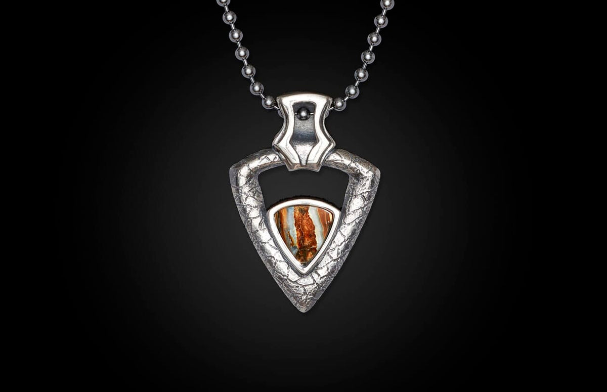 Silver-toned arrowhead pendant with a textured metal frame and a striped brown, orange, and white stone, hanging on a ball chain.