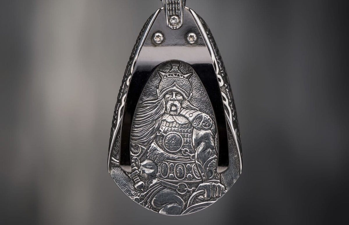 Silver-toned metal pendant featuring an intricately engraved warrior in a helmet, holding a sword.
