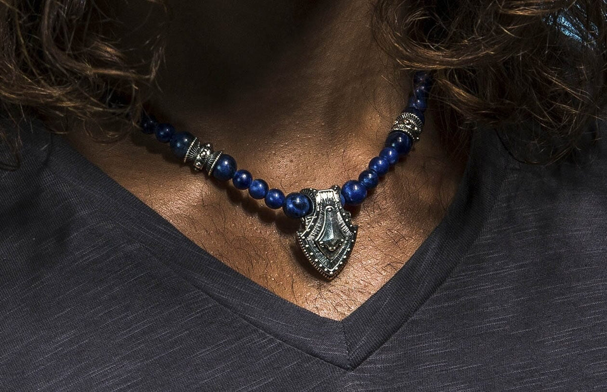 Sodalite shield necklace with blue beaded stones and a silver-toned shield pendant, worn on a person's neck.