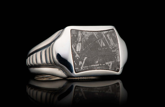 RING 8 MET - 13|Polished metal ring with a rectangular meteorite inlay showing a distinct crisscross pattern, reflected on a black surface.