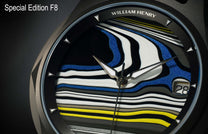 Special Edition Fordite watch by William Henry featuring blue, white, black, and yellow marbled dial with triangular hour markers and date window, close-up view