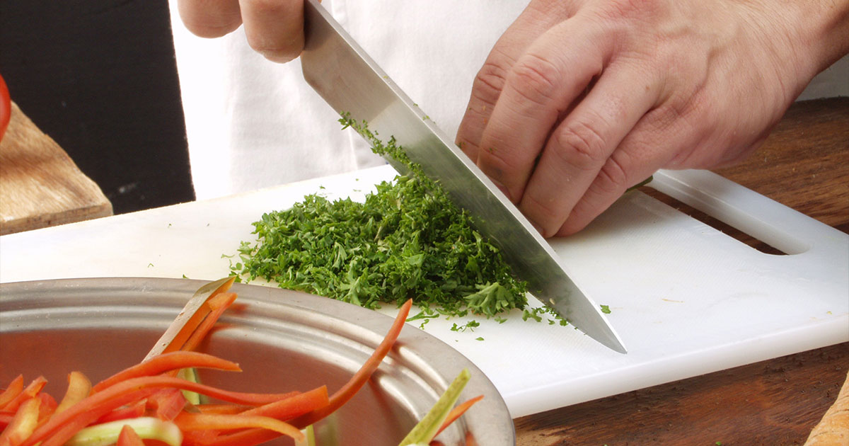 Chef cutting parsley with kitchen knife