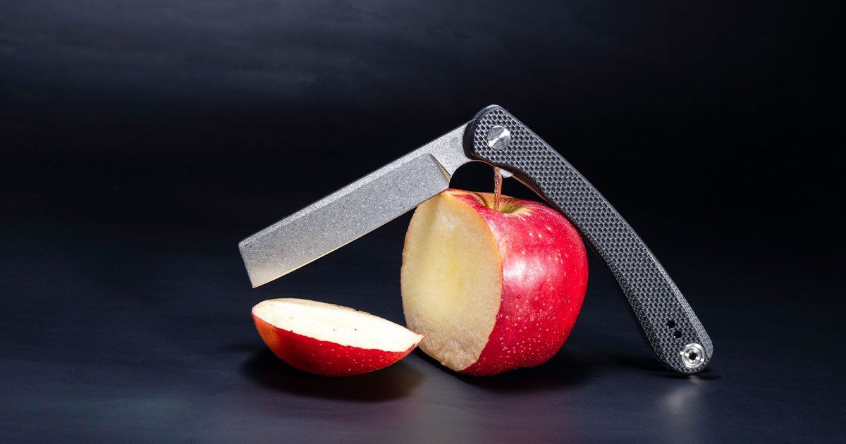 Black folding knife cutting apple